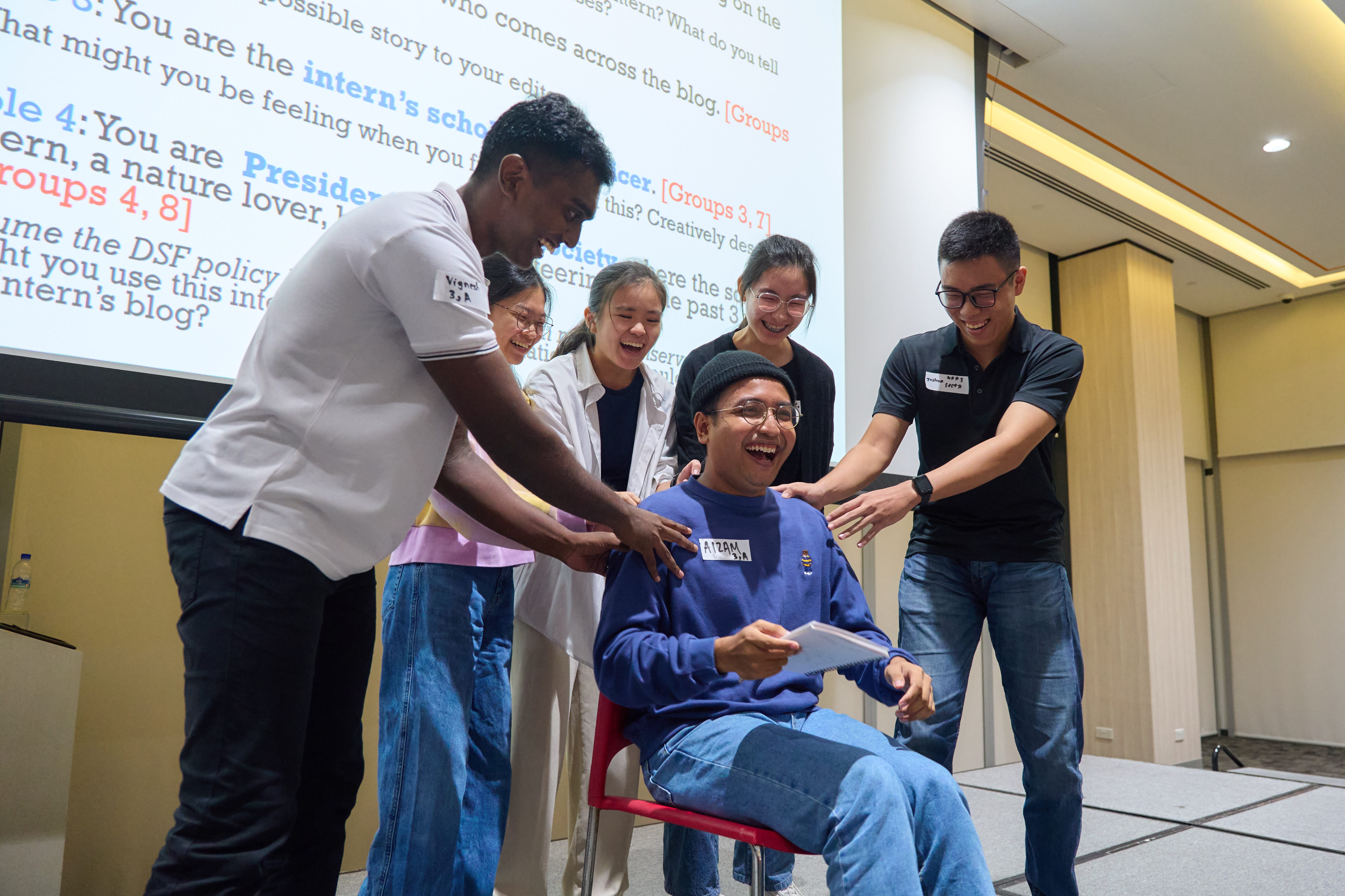 Group of scholars roleplaying with a one student sitting at the center and they all are laughing and having fun